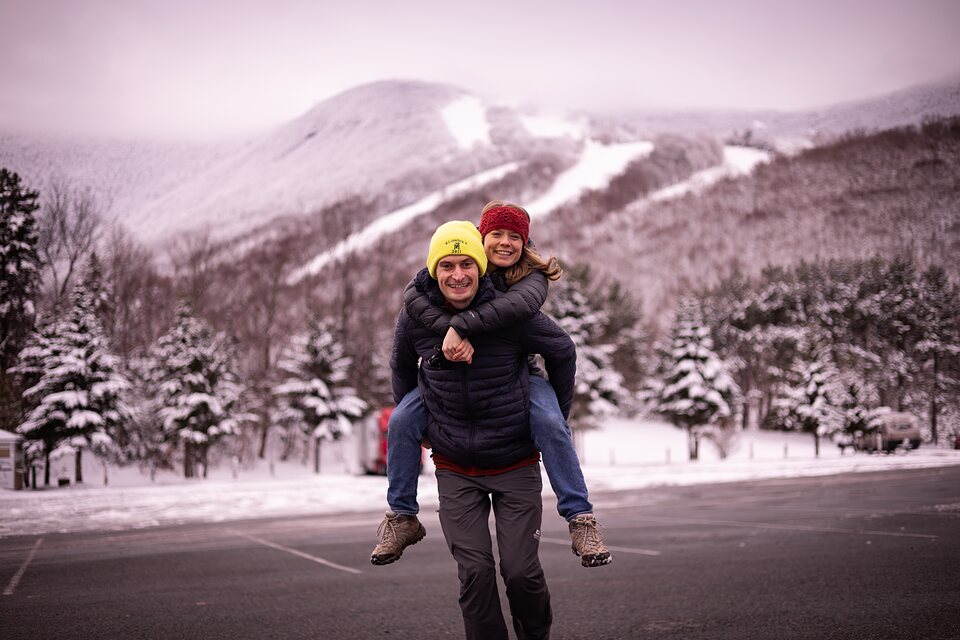 One partner carrying the other on their back in front of a snowy mountain