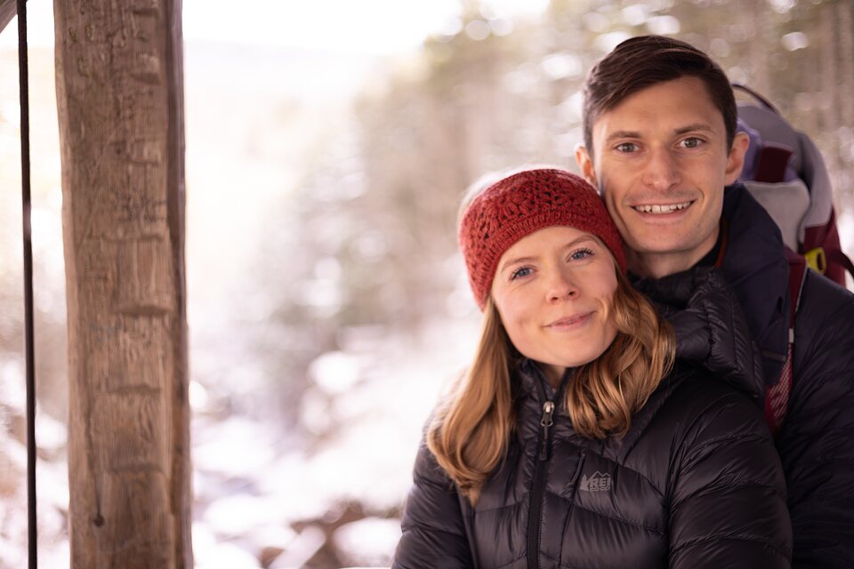 Close portrait of a couple in winter coats beside a wooden post
