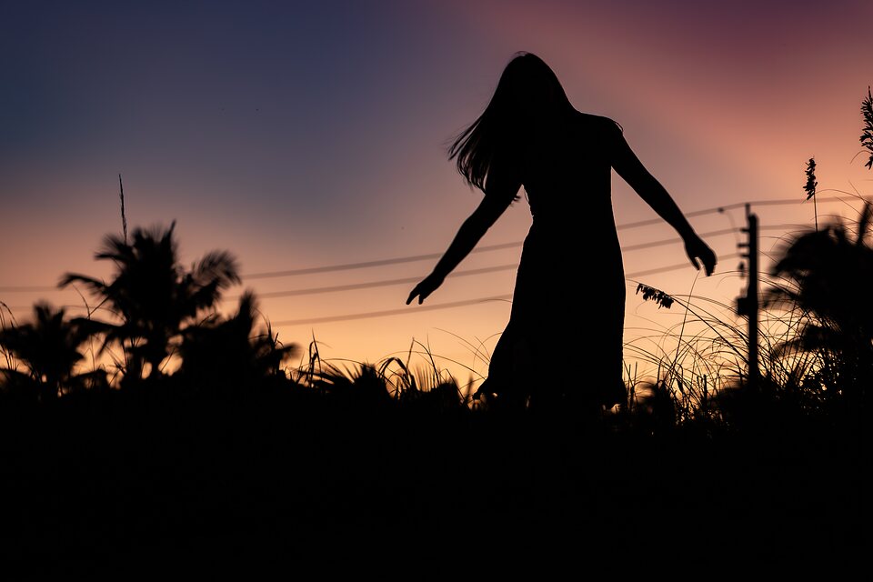 Silhouette of a woman reaching out through sea grass at sunset