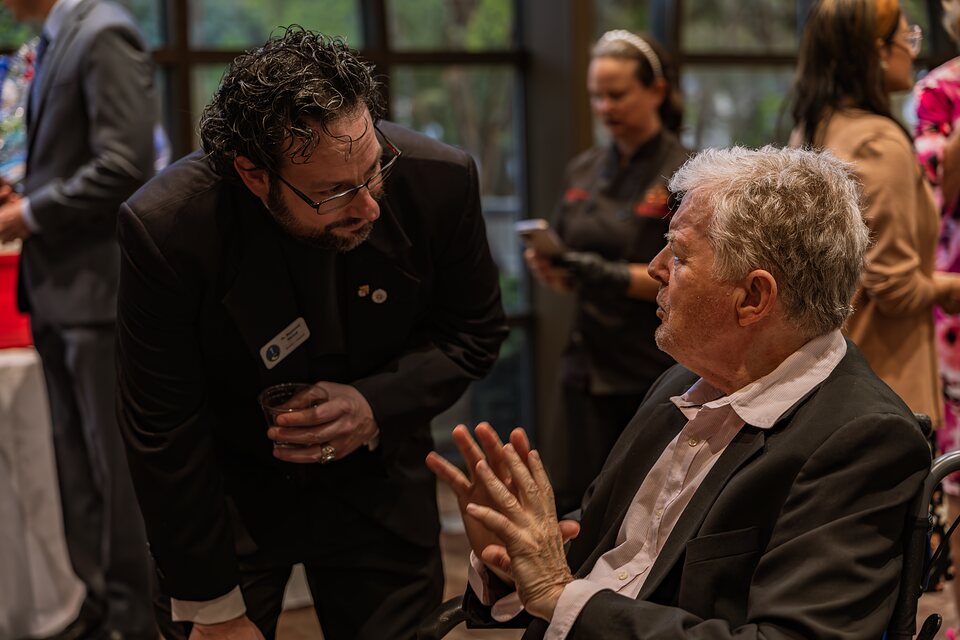 A priest crouching to talk with a seated guest during the reception