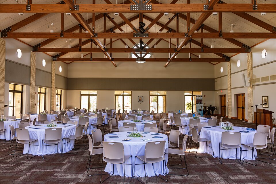 Banquet hall set with round tables beneath exposed wooden trusses before guests arrive
