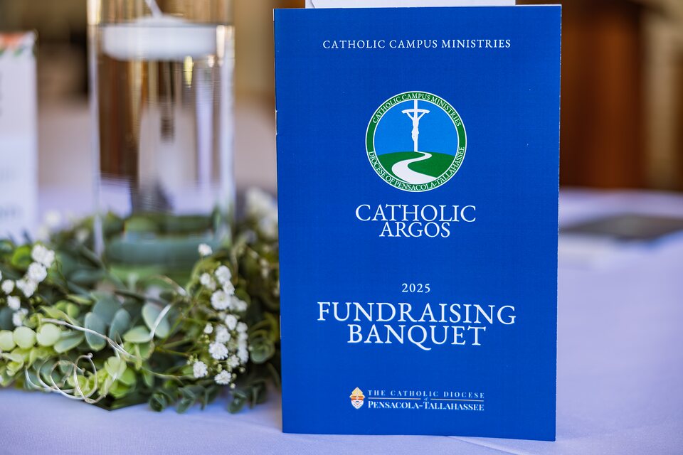 Event program standing beside a candle and greenery on a linen table