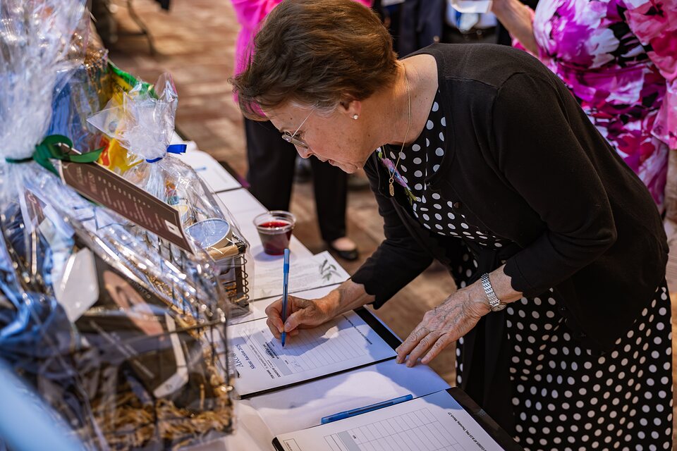 Guest leaning over a silent auction sheet to write a bid