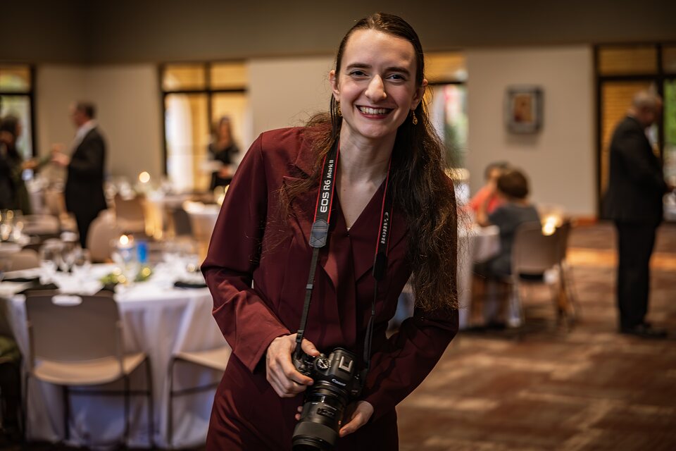 Grace holding her camera in the middle of an event she is photographing
