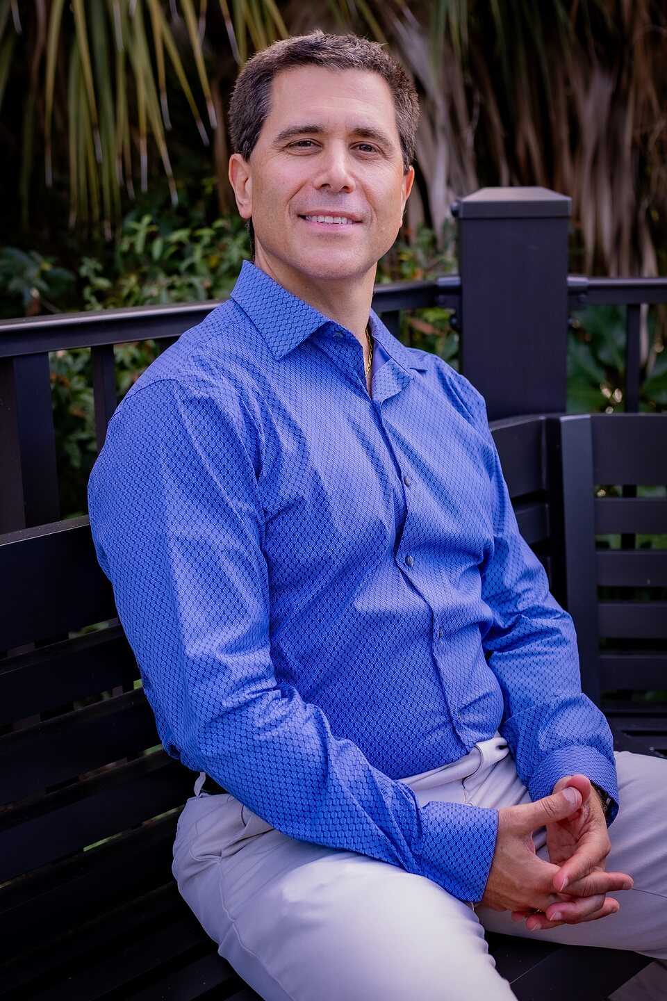 Professional portrait of a man seated on a bench among greenery