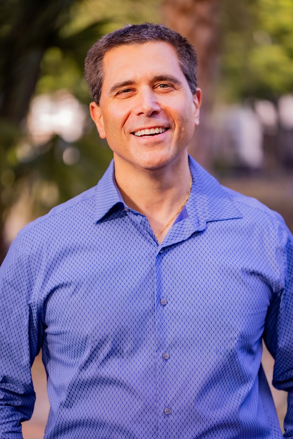 Outdoor professional headshot of a man in a blue shirt