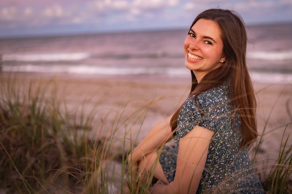 Young woman seated in beach grass at dusk, ocean behind her