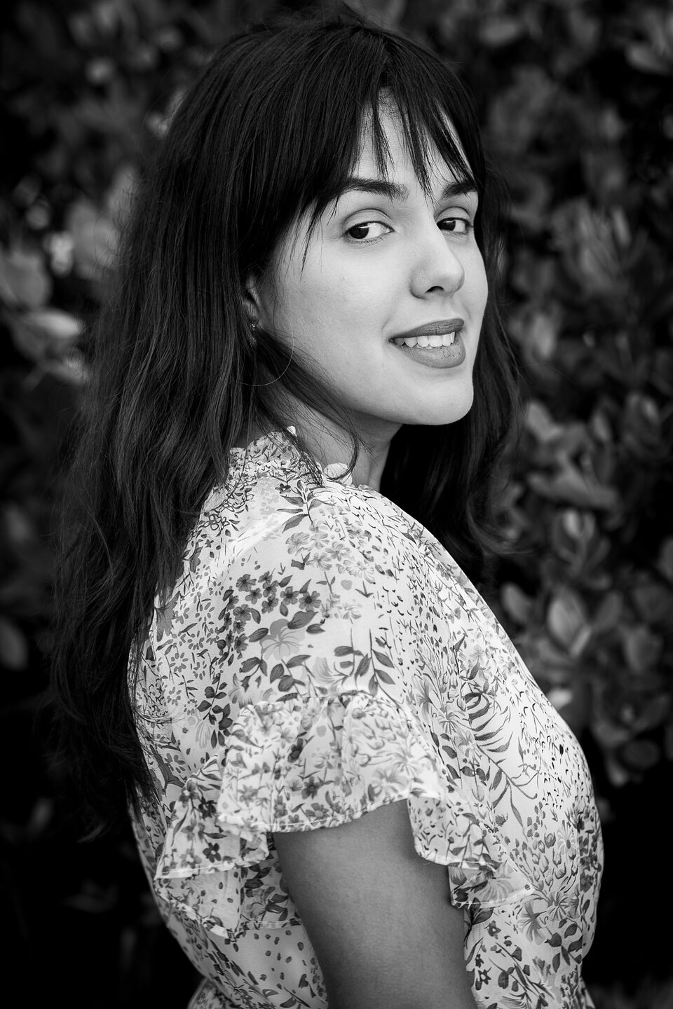 Black and white portrait of a woman turning to look over her shoulder against a hedge
