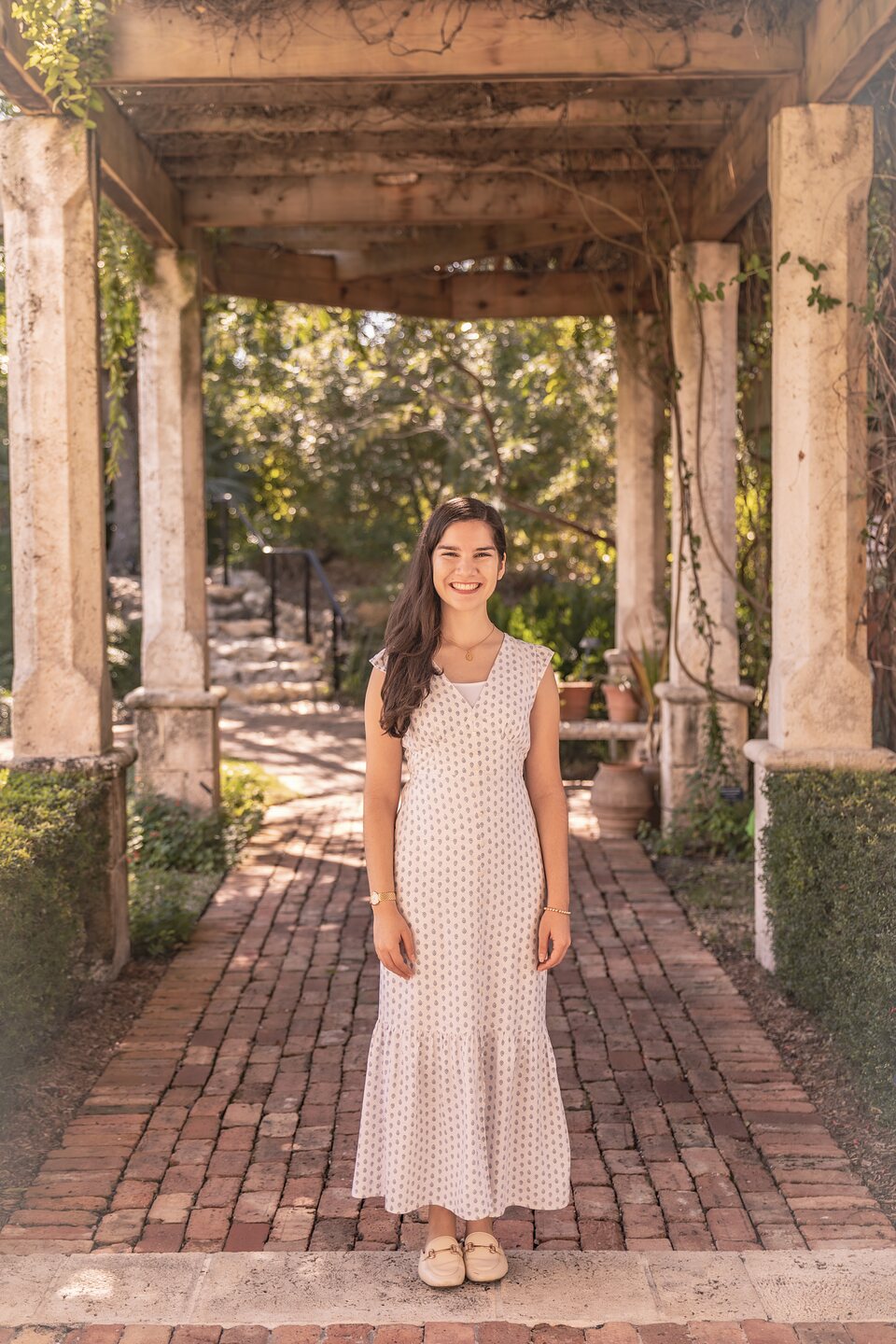 Full-length portrait on a brick path beneath a stone pergola