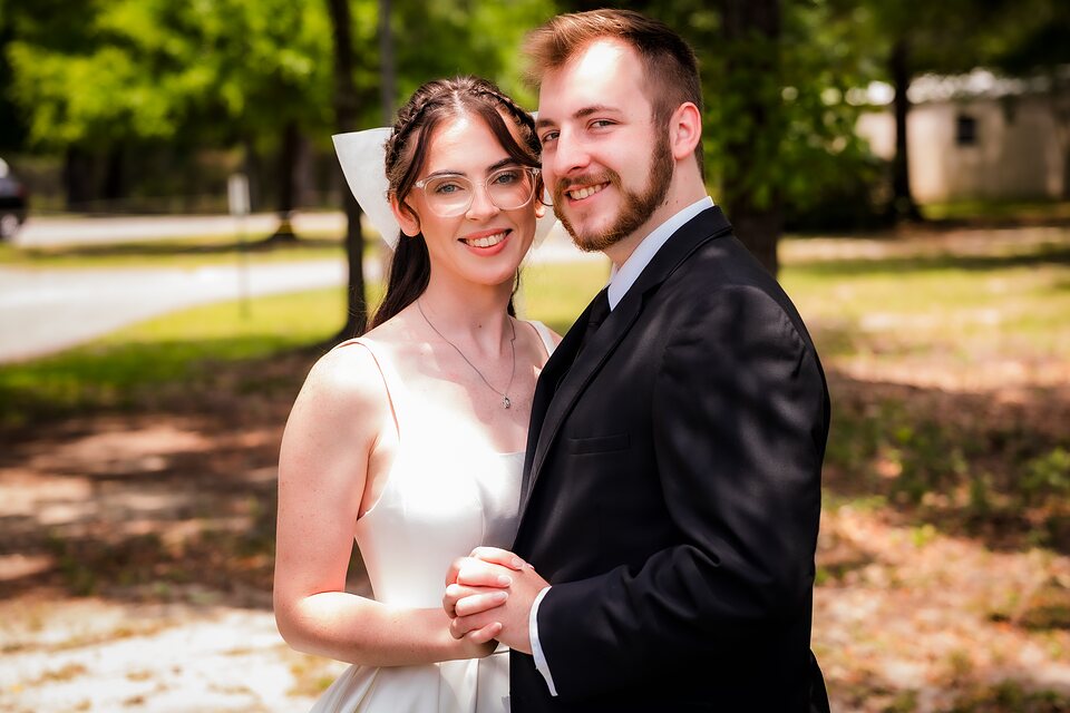 Newly married couple holding hands outdoors in dappled light