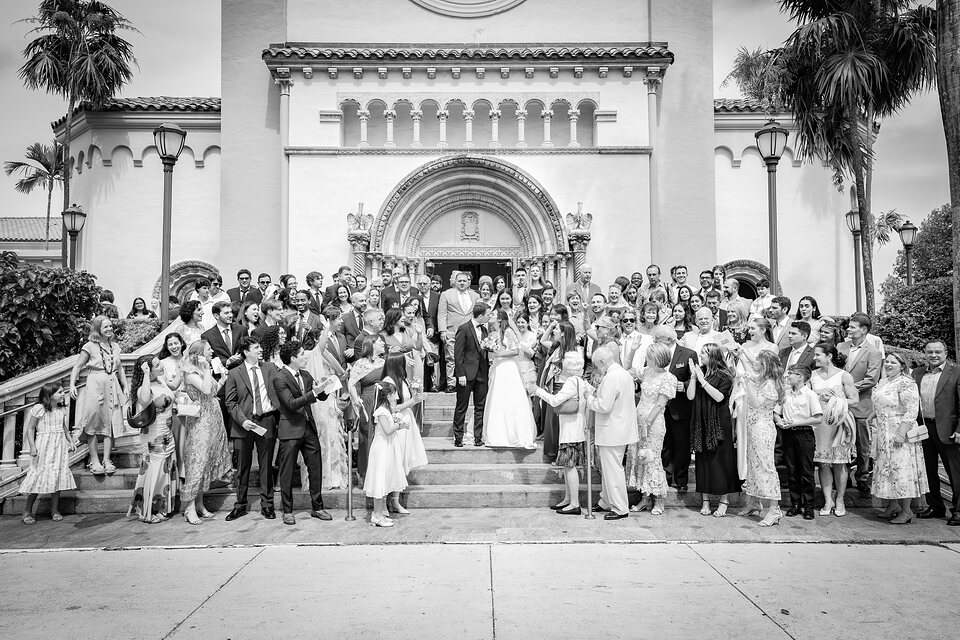 Wedding guests lining the church steps as the couple kiss at the centre