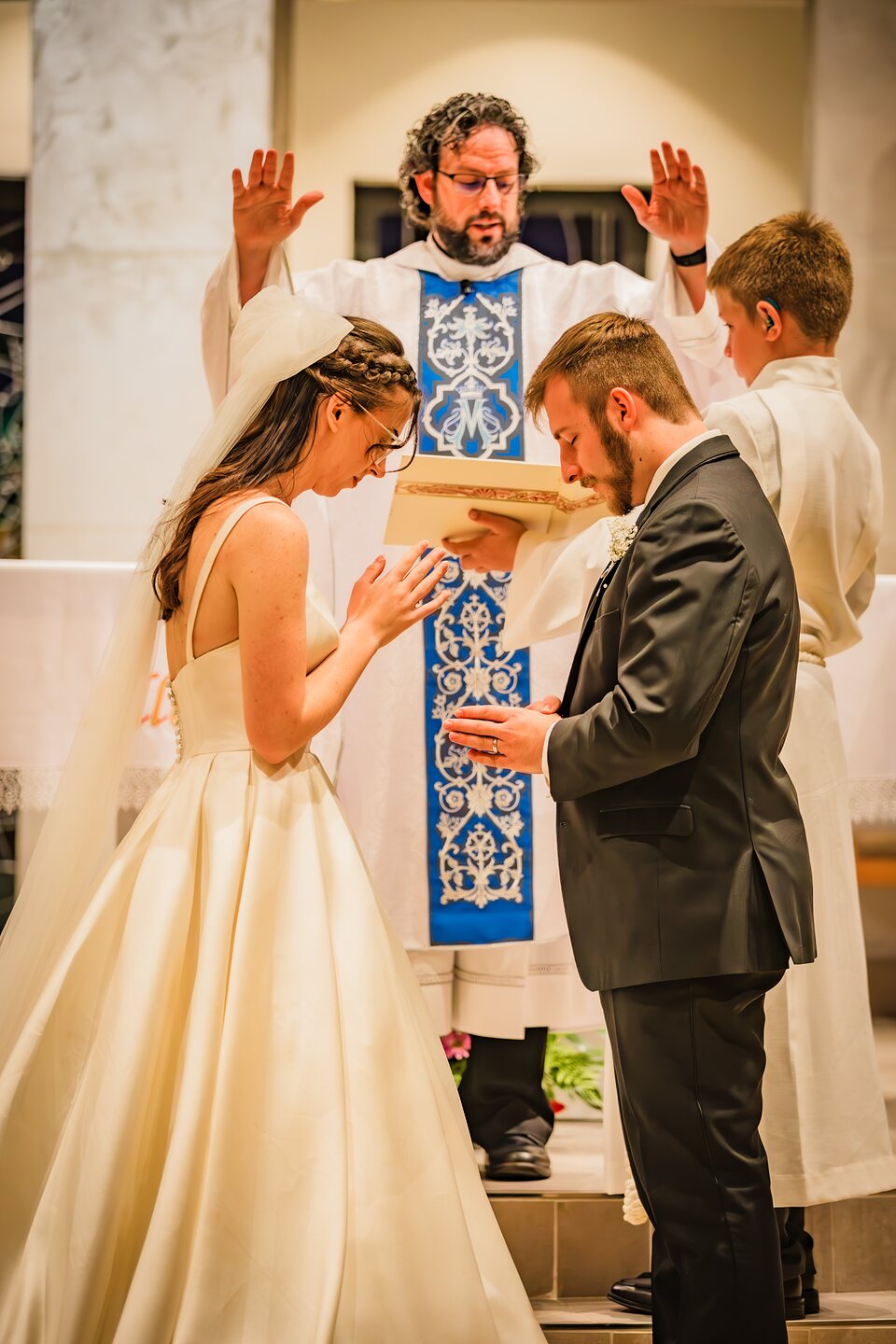 Bride and groom bowing their heads as the priest gives the nuptial blessing