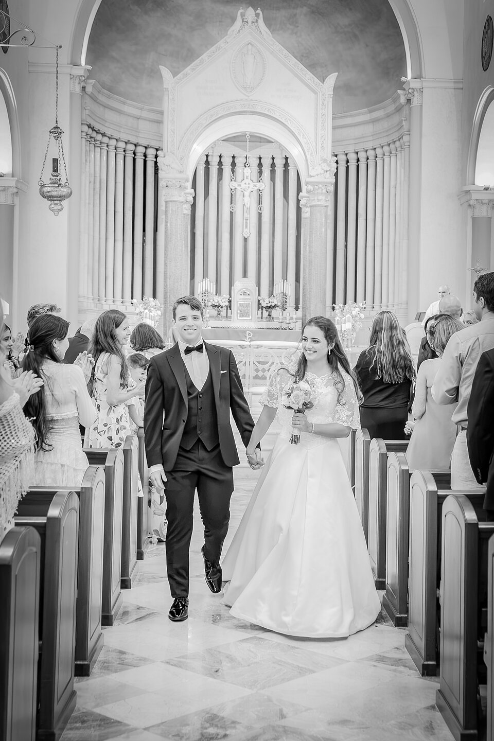 A newly married couple walking back down the aisle hand in hand as guests applaud