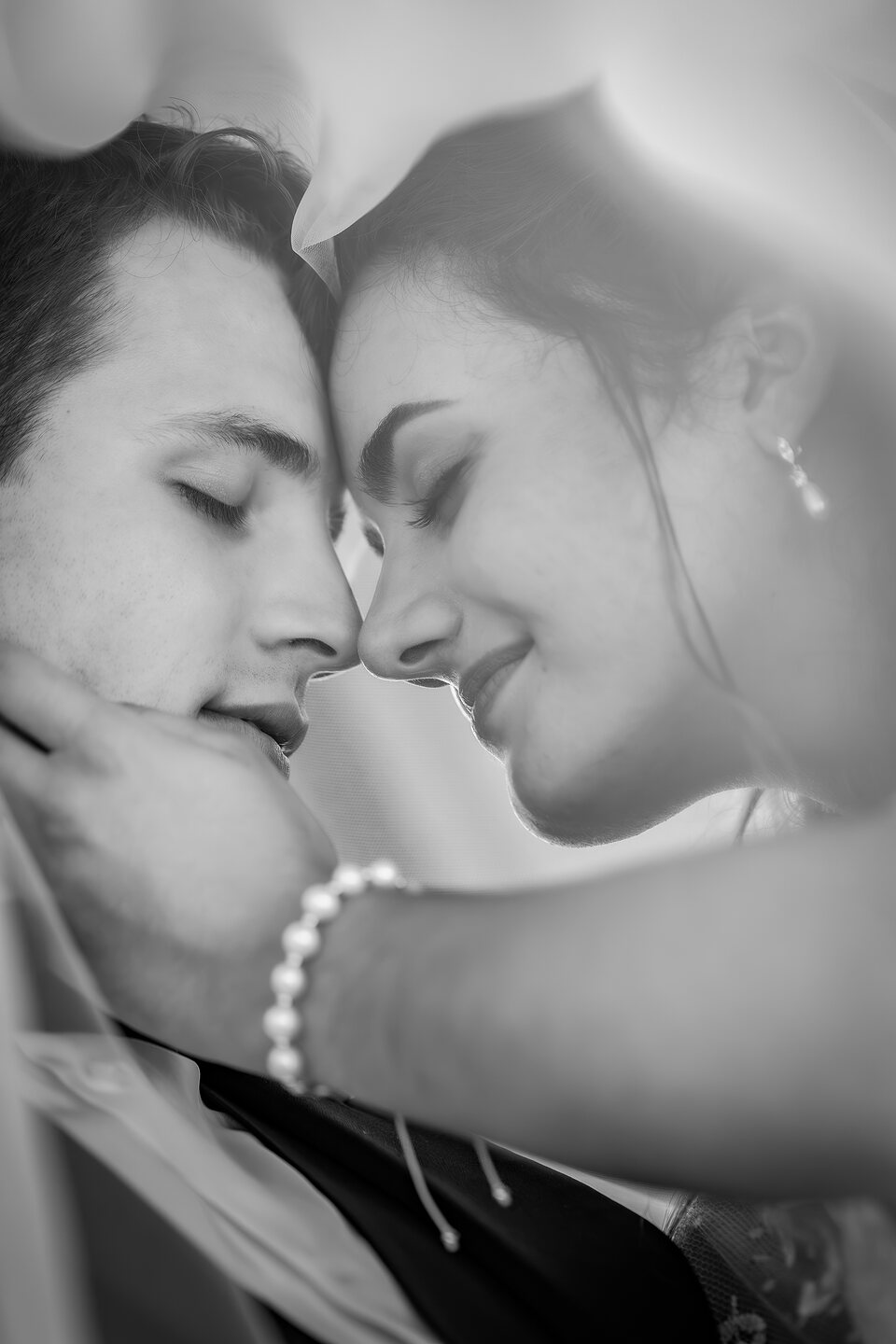 A bride and groom with their foreheads together beneath her veil, eyes closed